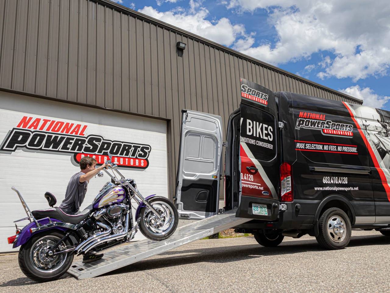 A motorcycle being loaded into a National Powersports Distributors delivery van outside the dealership