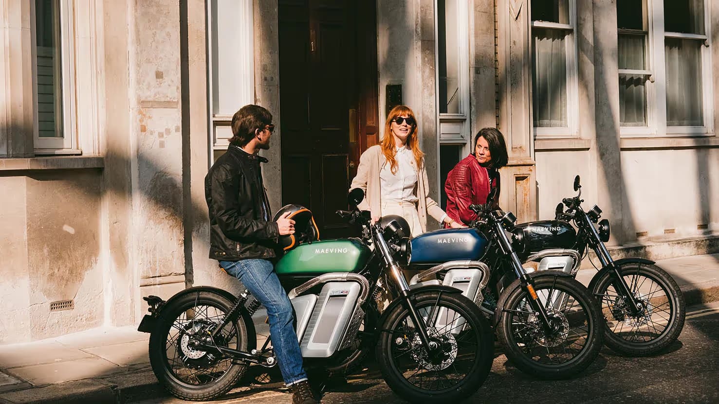 Three riders standing with Maeving electric motorcycles outside a townhouse